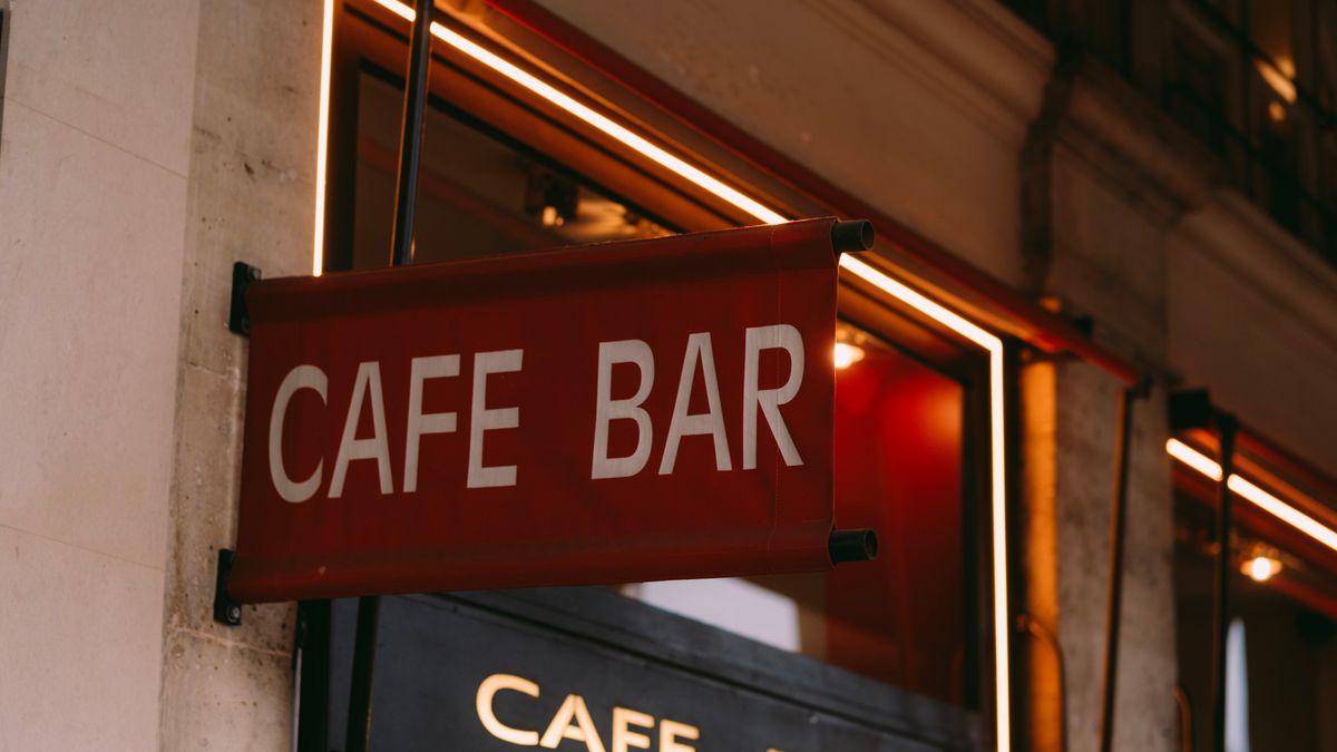 Stylish cafe bar sign illuminated with neon lights in urban setting.