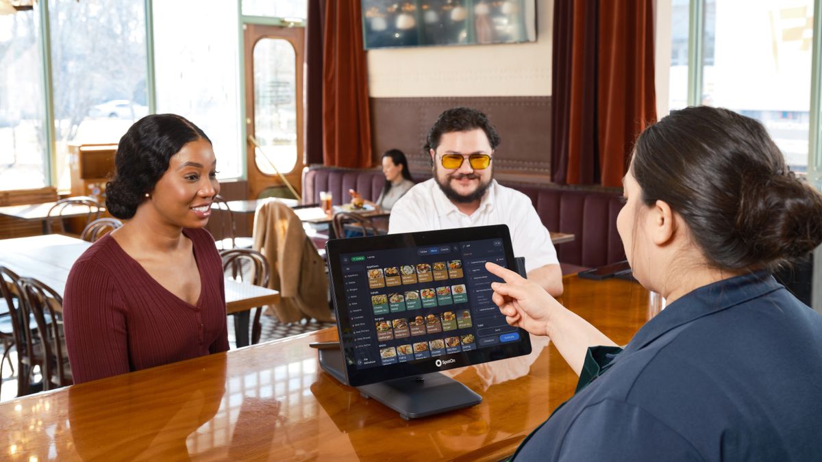 Server demonstrating a SpotOn POS system for customers in a cozy restaurant setting.