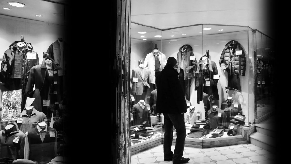 Man admiring fashion display through a clothing store window in black and white.