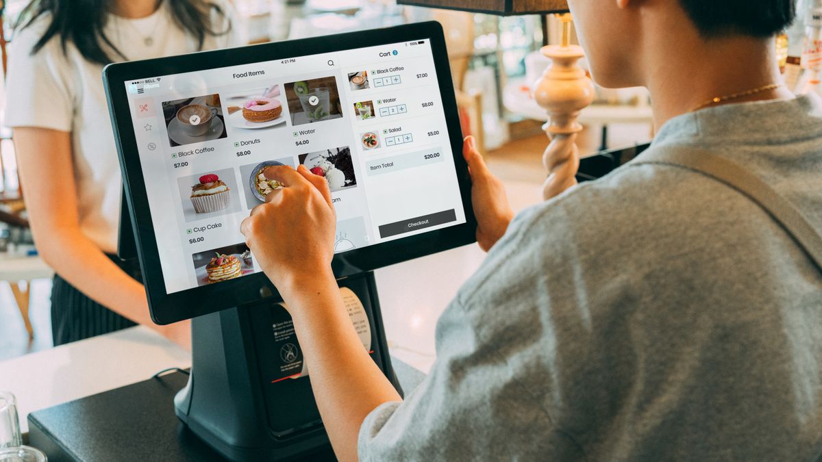 A customer using a touch screen system at a cafe counter for modern payment processing.