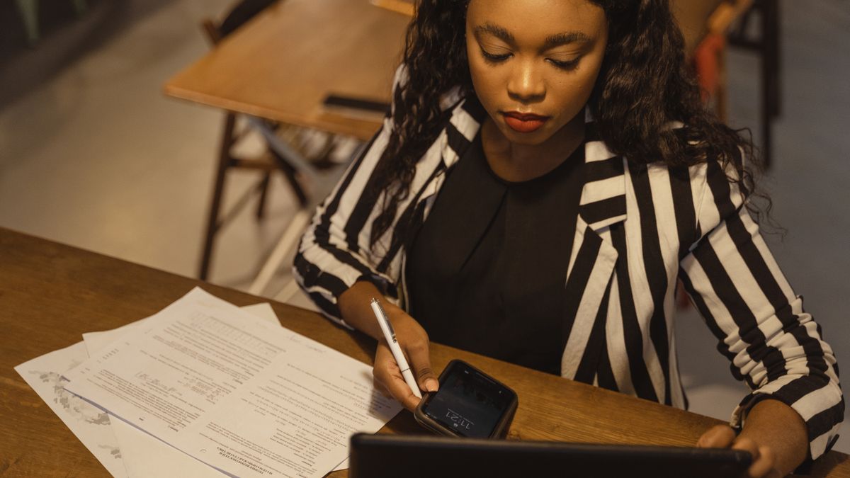 Focused woman in business attire working on a laptop with paperwork at a desk.
